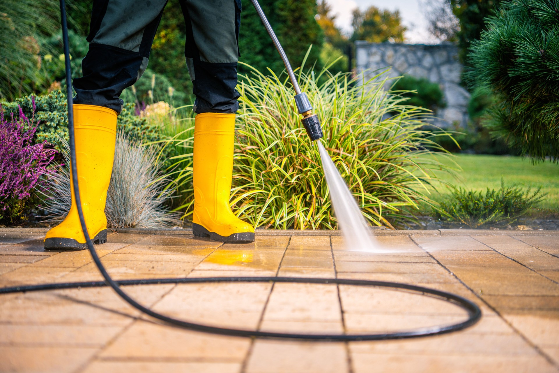 Person Using a Pressure Washer on a Patio Surrounded by Greenery During Daytime